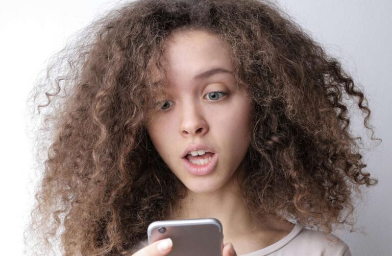 ragazza giovane con capelli ricci guarda smartphone con espressione sorpresa concetto di cringe