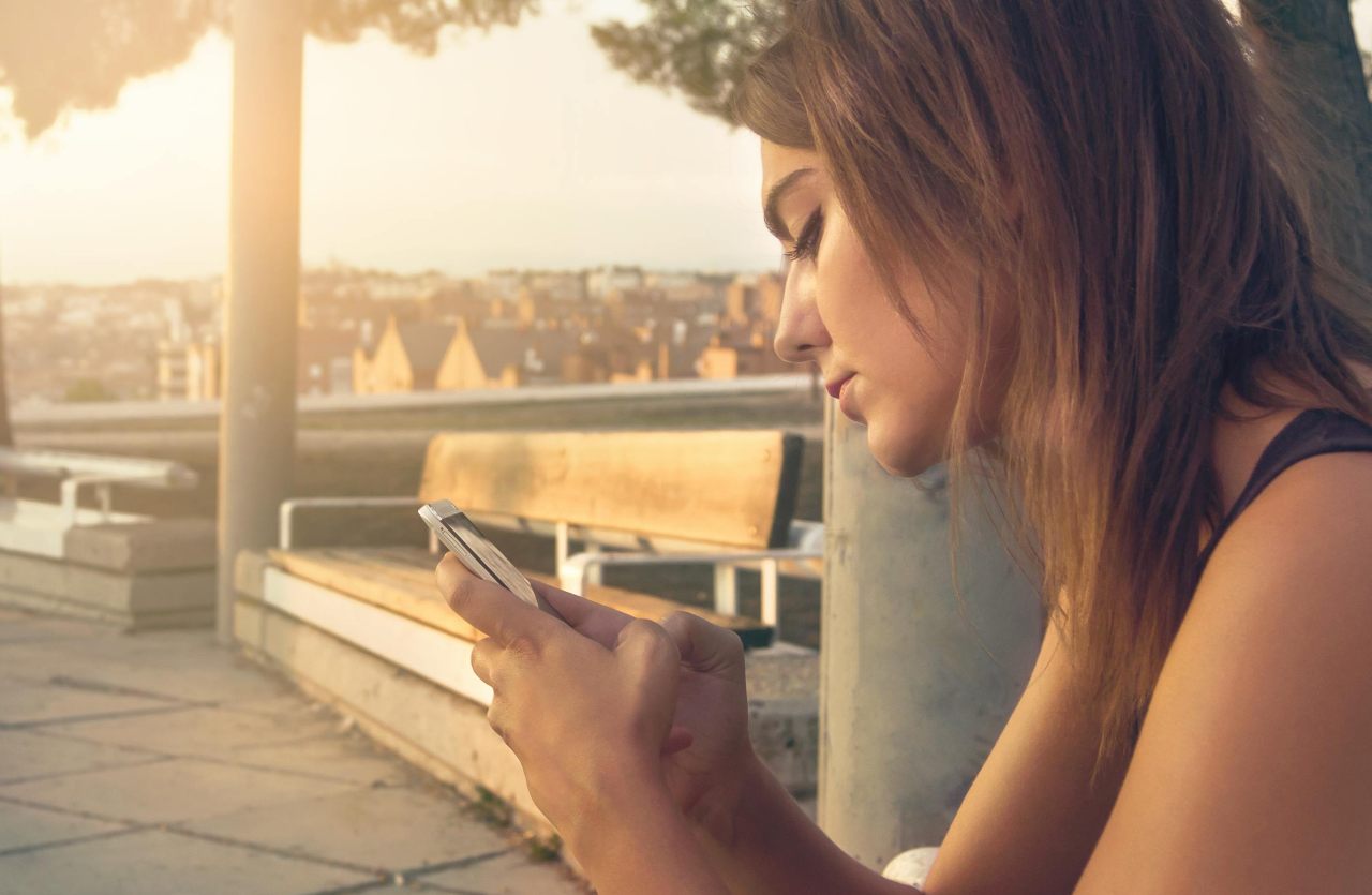 Ragazza di profilo guarda lo smartphone all'aperto con espressione triste concetto di ghosting