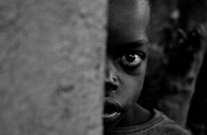Beasts of No Nation recensione: primo piano in bianco e nero dello sguardo spaventato di un bambino che si nasconde dietro un muro