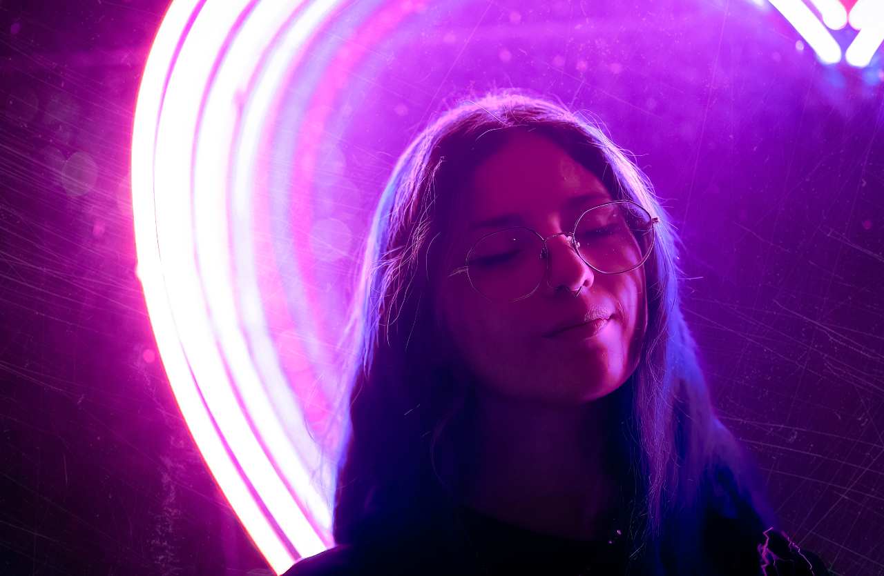 Ragazza con occhiali e occhi chiusi illuminata da un neon circolare viola, concetto di visualizzazione mentale e neuroplasticità
