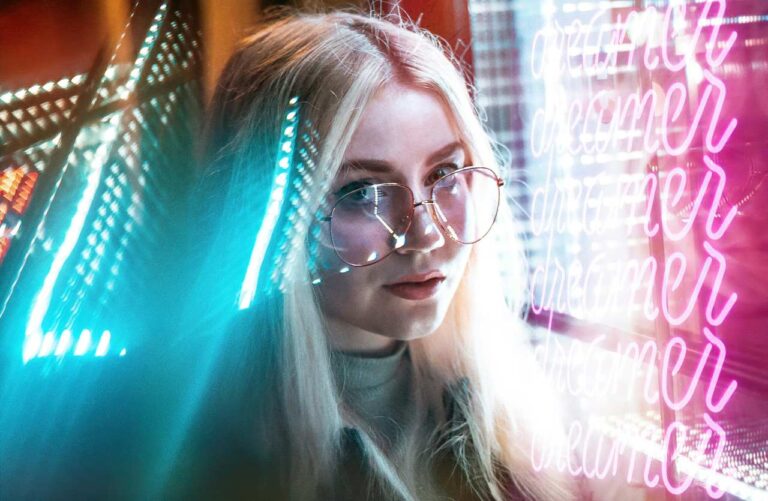 Ragazza bionda con occhiali davanti a una scritta neon dreamer, focus sui concetti di manifesting e attenzione selettiva