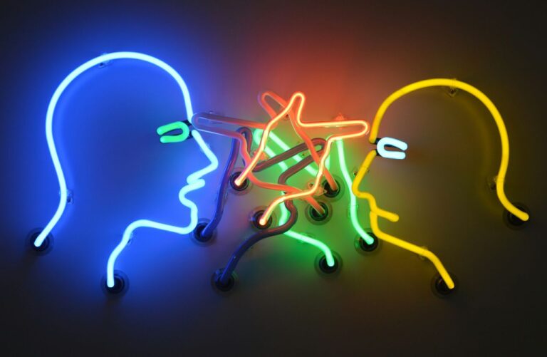 Installazione al neon con due volti stilizzati e luci confuse al centro, usata come concetto di salute mentale