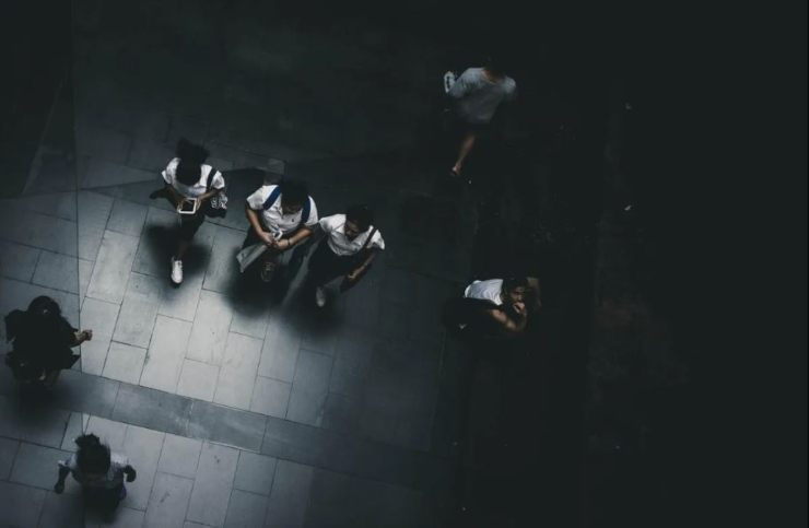 Inquadratura dall'alto di studentesse in divisa scolastica che camminano su un pavimento di pietra grigia tra ombre profonde