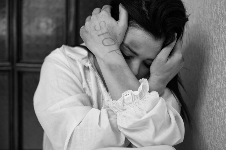 Foto in bianco e nero di una donna che si copre il volto con le mani, mostrando lividi sulle braccia e la scritta "STOP" sul palmo della mano.