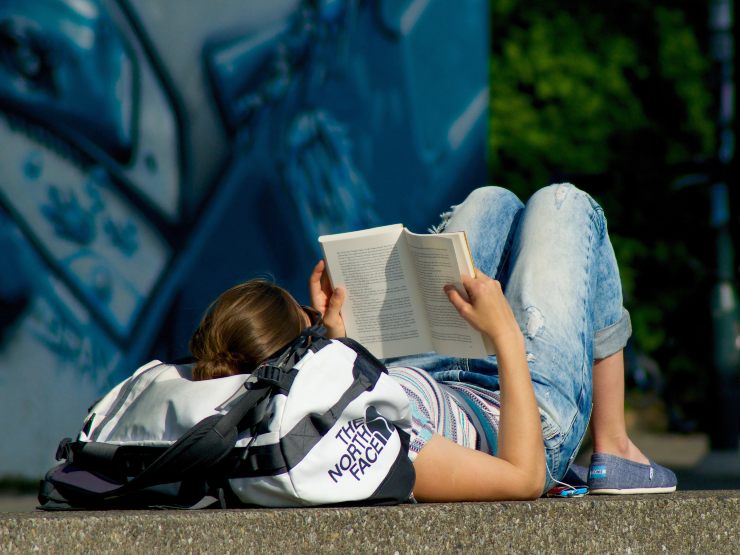 ragazza distesa sull'asfalto che legge un libro